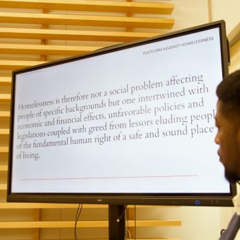 Photo from YMCA Homeinclusration study launch of a speaker standing next to a power point presentation.