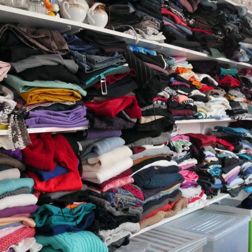 The Charity & Vintage Shop located in Żabbar promotes a circular economy and sustainability, and helps fundraise for our community services. This is an image of inside the YMCA Charity & Vintage Shop. It shelves full of various shirts and jumpers.